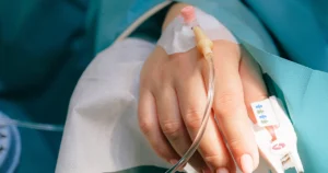 Patient in critical condition lying in a hospital bed with an IV drip attached to their hand, symbolizing the need for critical illness coverage.